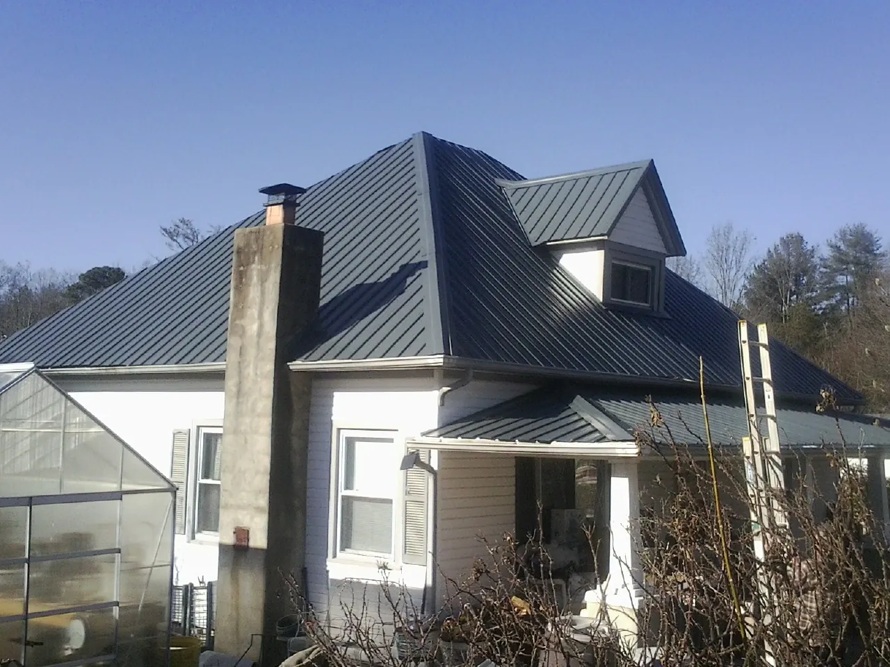 Dark blue standing seam metal roof on a white farmhouse with dormer — Slate & Tile Roof Repair by Roofing Brothers in Bryan
