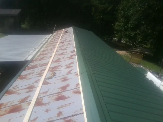 Old rusted panels beside newly installed green metal roofing in Bryan