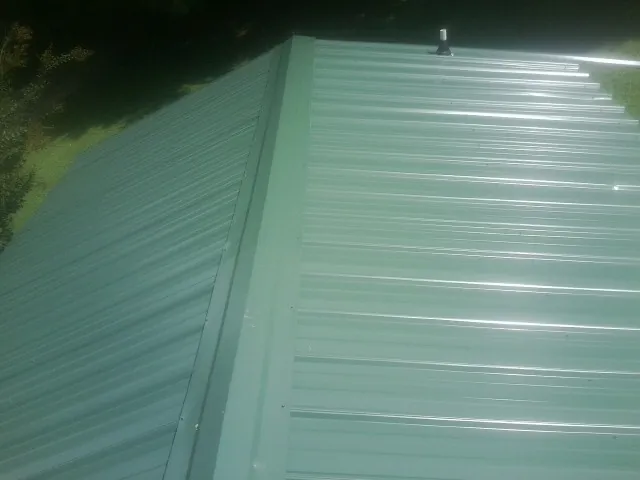 New green metal panels meeting at the ridge of a roof — Flat Roof Repair work by our crew in Bryan
